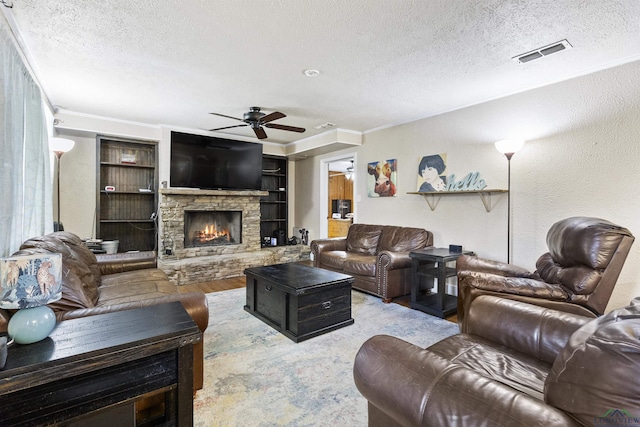 living room with a stone fireplace, ceiling fan, built in features, a textured ceiling, and ornamental molding