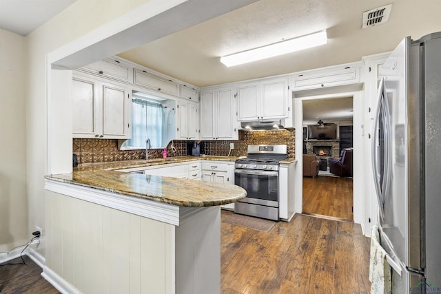 kitchen featuring white cabinetry, sink, stainless steel appliances, kitchen peninsula, and dark stone counters