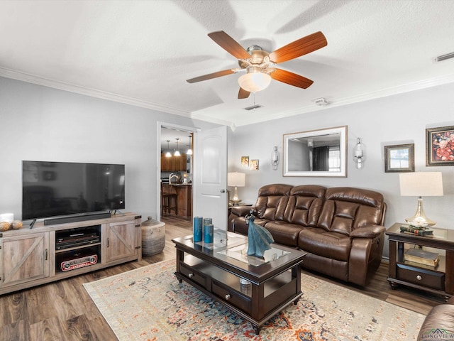 living area with a ceiling fan, a textured ceiling, ornamental molding, and wood finished floors