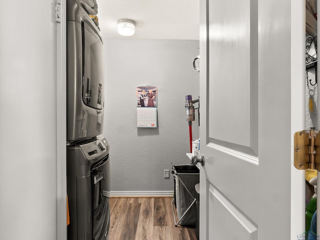 laundry room featuring laundry area, baseboards, a textured wall, stacked washer and clothes dryer, and wood finished floors