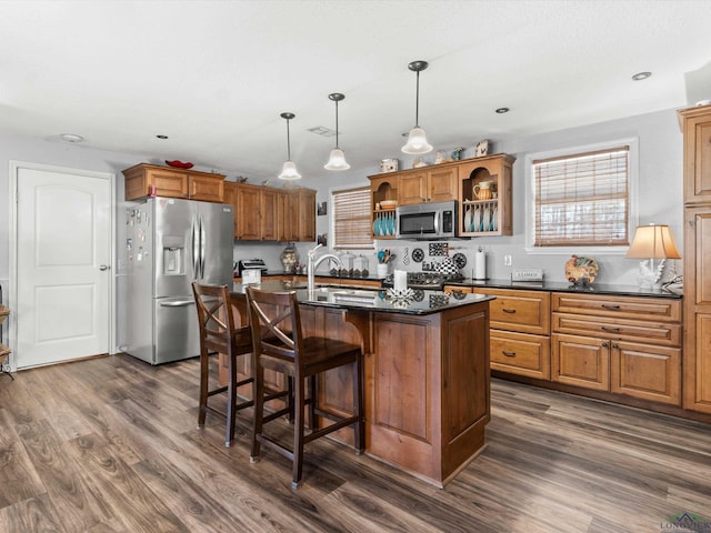 kitchen featuring appliances with stainless steel finishes, dark wood-type flooring, brown cabinetry, and a kitchen breakfast bar