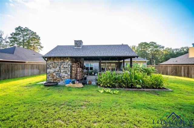 back of house with stone siding, a lawn, and a fenced backyard