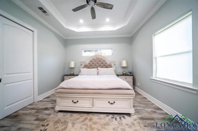 bedroom with a raised ceiling, visible vents, light wood-style flooring, and baseboards