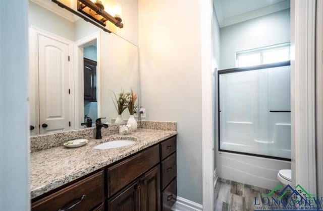 full bath featuring crown molding, bath / shower combo with glass door, vanity, wood finished floors, and baseboards