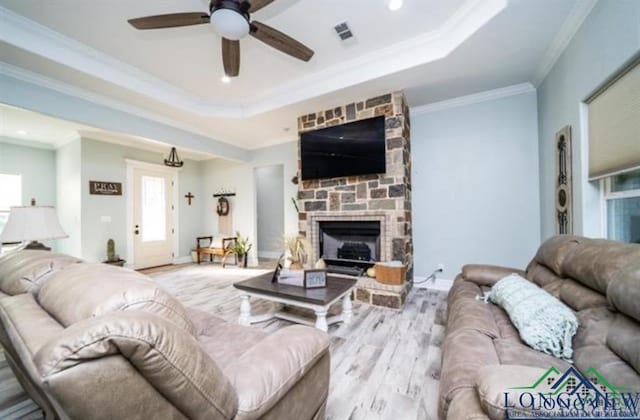 living room featuring crown molding, a raised ceiling, a fireplace, and light wood finished floors