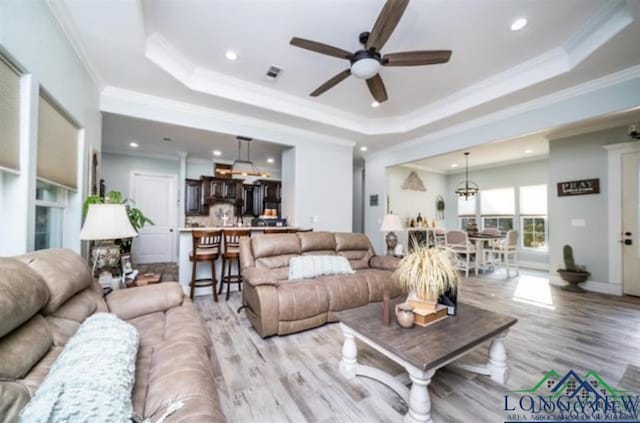 living room featuring a tray ceiling, visible vents, crown molding, and light wood-style flooring