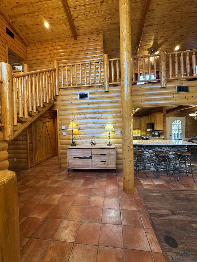 unfurnished living room with wooden ceiling, ceiling fan, a towering ceiling, log walls, and beamed ceiling