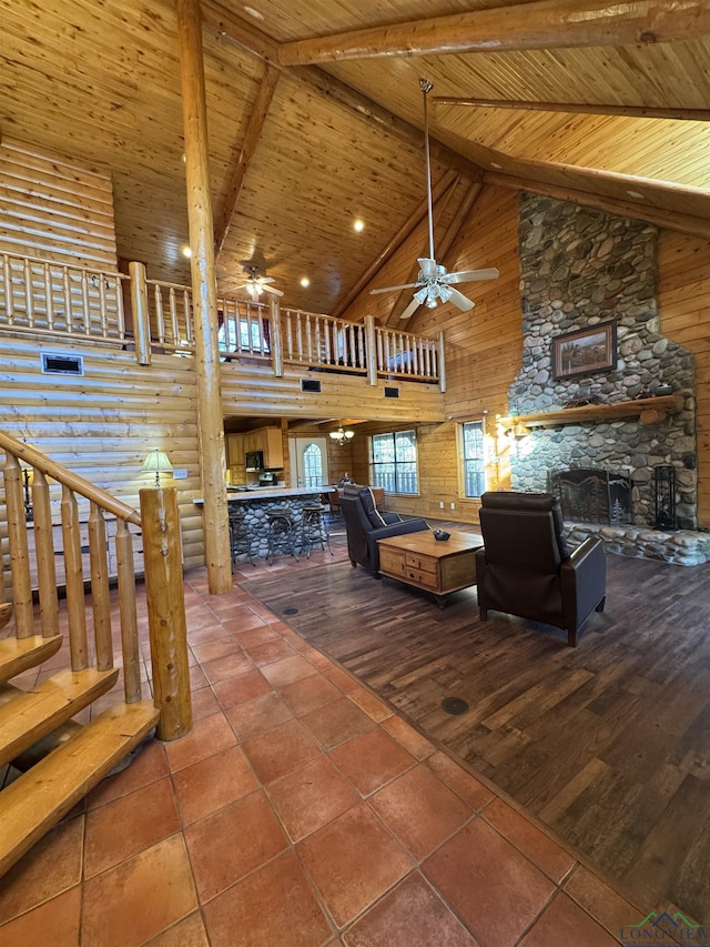 unfurnished living room with ceiling fan, log walls, a stone fireplace, high vaulted ceiling, and wood ceiling