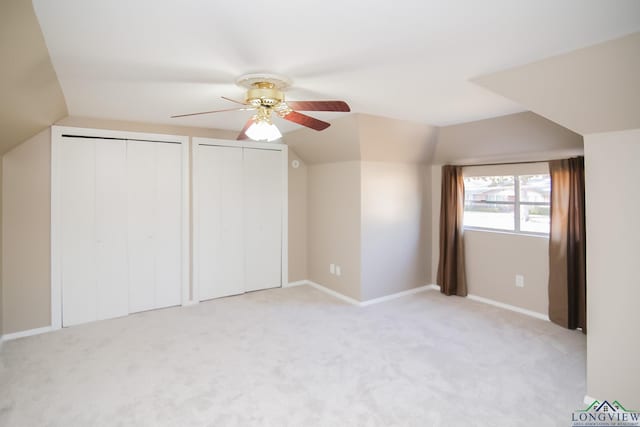 unfurnished bedroom featuring multiple closets, light colored carpet, lofted ceiling, and a ceiling fan