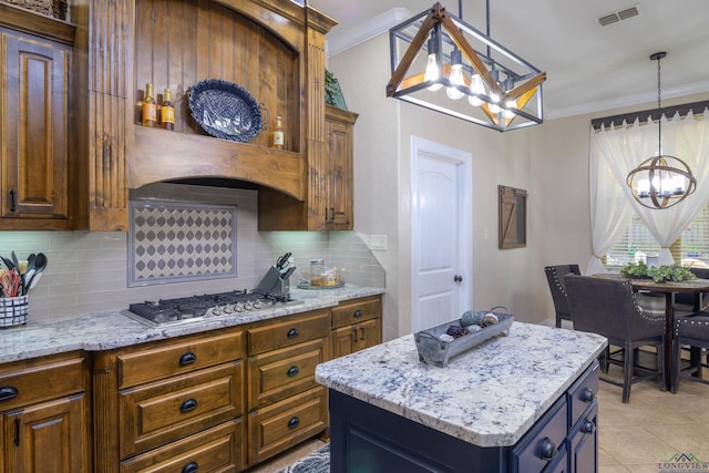 kitchen with stainless steel gas stovetop, a center island, tasteful backsplash, a notable chandelier, and light stone counters