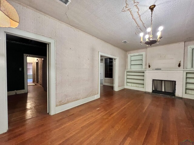 unfurnished living room with an inviting chandelier, a brick fireplace, built in features, a textured ceiling, and wood-type flooring