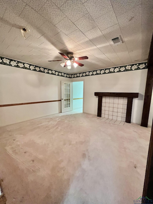 empty room with carpet, a tile fireplace, and ceiling fan