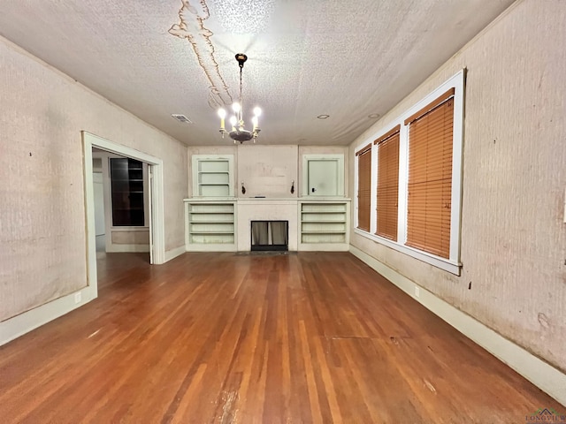 unfurnished living room with built in shelves, a textured ceiling, an inviting chandelier, and wood-type flooring