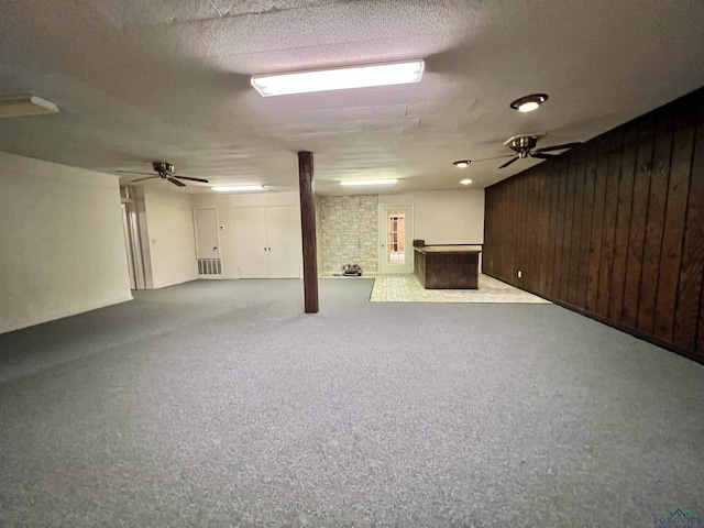 basement with a textured ceiling, ceiling fan, and wood walls