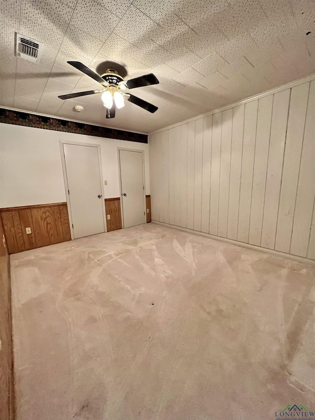 empty room featuring carpet flooring, ceiling fan, and wood walls