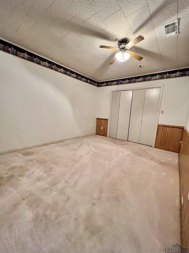 unfurnished bedroom with carpet flooring, a closet, ceiling fan, and wooden walls