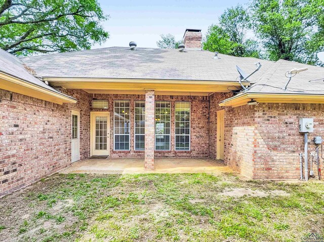 rear view of house with a patio, a shingled roof, brick siding, and a chimney