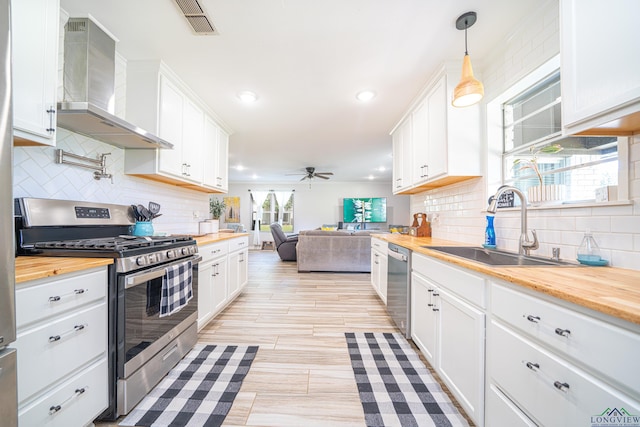 kitchen with white cabinetry, wall chimney exhaust hood, butcher block countertops, pendant lighting, and appliances with stainless steel finishes