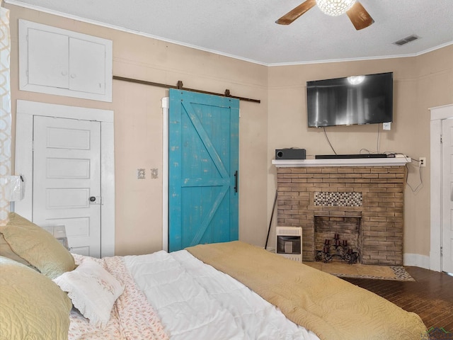 bedroom with visible vents, heating unit, wood finished floors, a barn door, and a brick fireplace