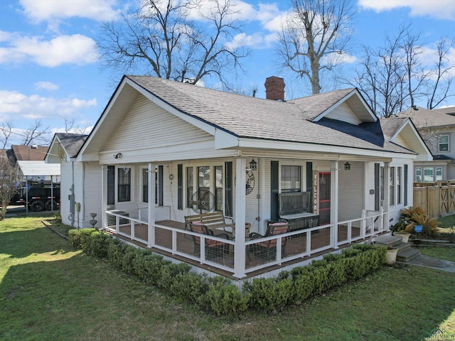 view of front facade featuring a chimney, a porch, a shingled roof, and a front lawn