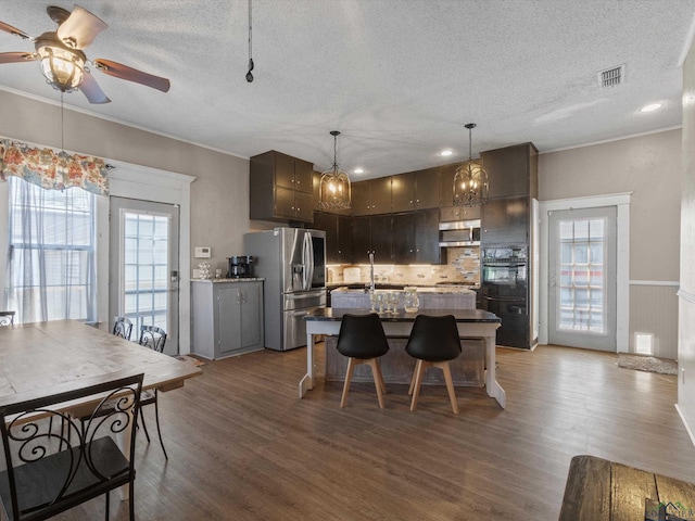 kitchen featuring stainless steel appliances, a textured ceiling, visible vents, and wood finished floors