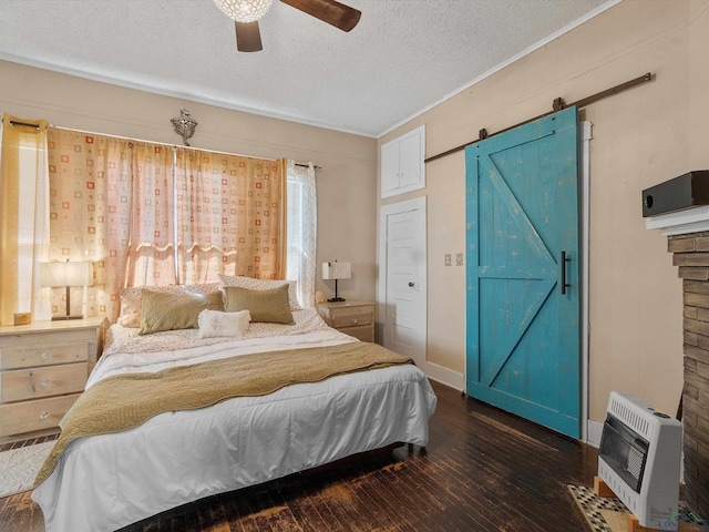 bedroom with ceiling fan, a barn door, hardwood / wood-style floors, heating unit, and a textured ceiling