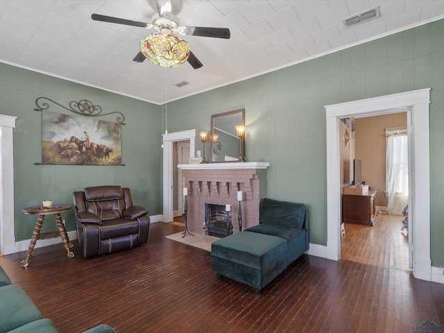 living area with hardwood / wood-style flooring, a brick fireplace, crown molding, and visible vents