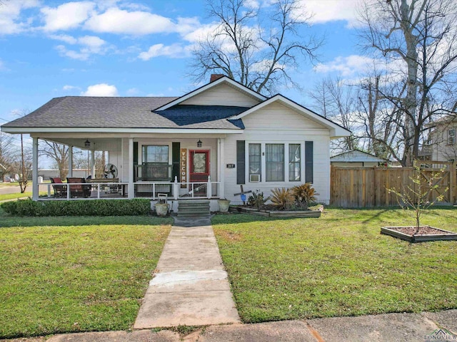 view of front facade with a front yard, fence, covered porch, and a shingled roof