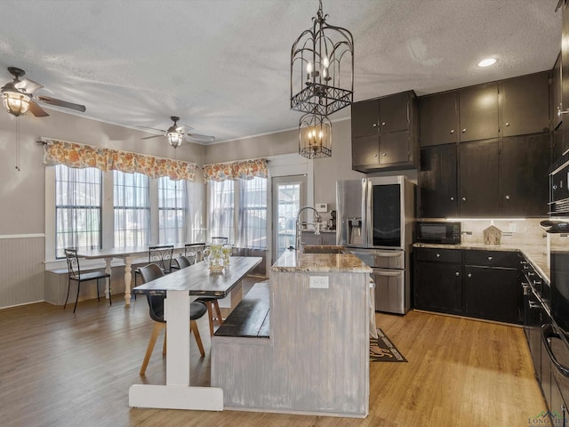 kitchen featuring black microwave, light wood-type flooring, light stone counters, stainless steel fridge, and a sink