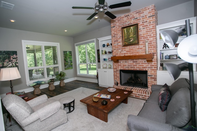 living room with hardwood / wood-style floors, ceiling fan, built in features, and a brick fireplace