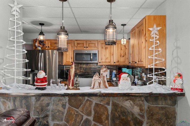 kitchen with appliances with stainless steel finishes, a paneled ceiling, tasteful backsplash, and hanging light fixtures