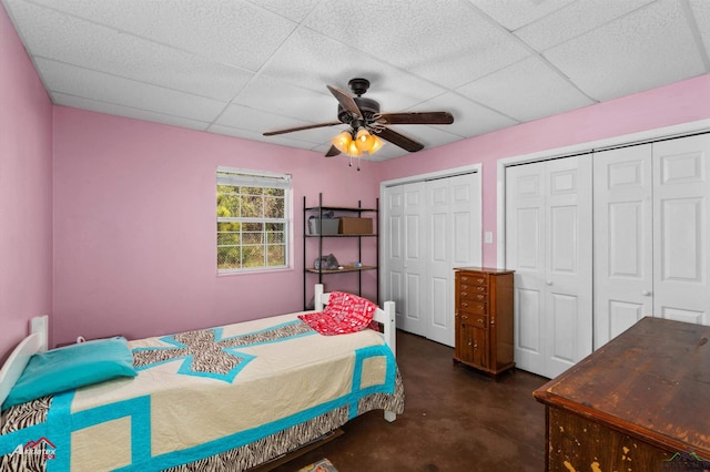 bedroom featuring a paneled ceiling, ceiling fan, and multiple closets