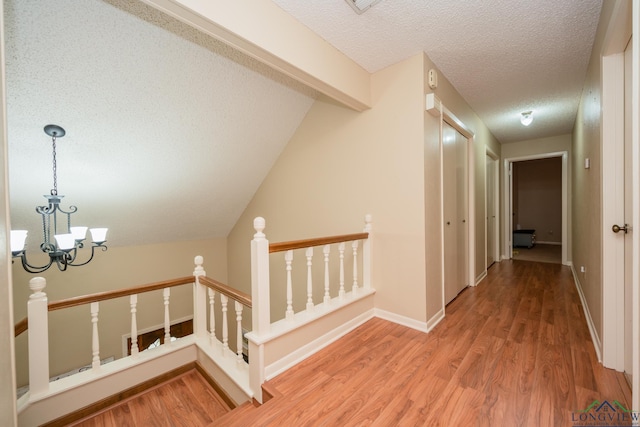 1002 Ruby St, Gilmer, TX 75644 - hallway with wood finished floors, a textured ceiling, a notable chandelier, and an upstairs landing