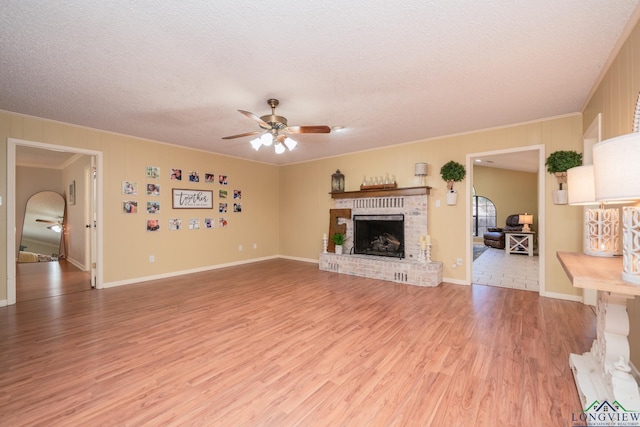 1002 Ruby St, Gilmer, TX 75644 - unfurnished living room featuring light wood finished floors, a ceiling fan, ornamental molding, a fireplace, and a textured ceiling