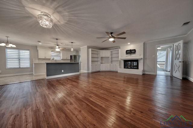 unfurnished living room with ornamental molding, dark hardwood / wood-style flooring, ceiling fan with notable chandelier, and a fireplace