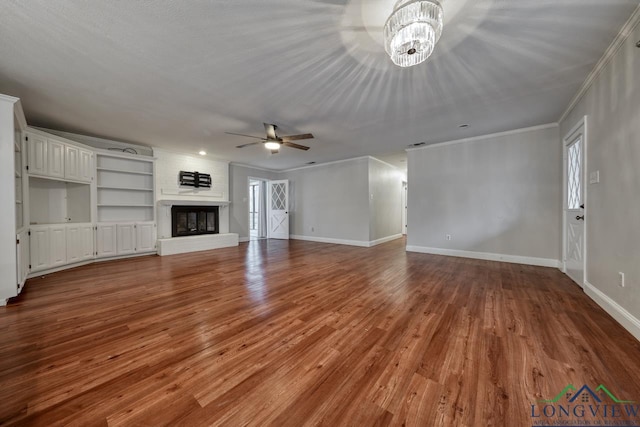 unfurnished living room with hardwood / wood-style flooring, crown molding, a brick fireplace, and ceiling fan with notable chandelier