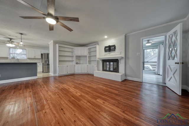 unfurnished living room with sink, crown molding, wood-type flooring, ceiling fan, and a fireplace