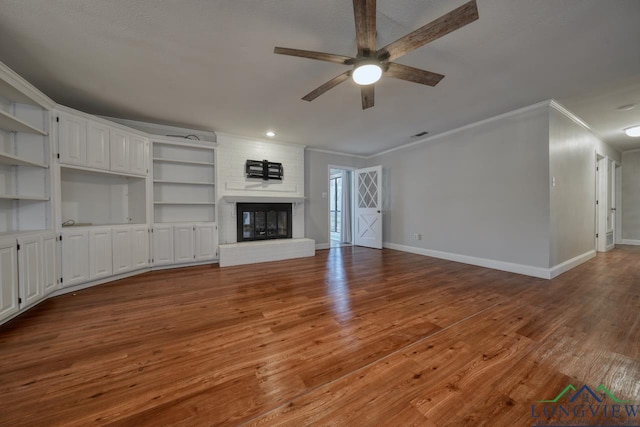 unfurnished living room featuring wood-type flooring, ornamental molding, ceiling fan, and a fireplace