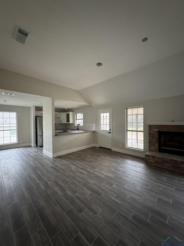 unfurnished living room featuring lofted ceiling, sink, a fireplace, and dark hardwood / wood-style floors