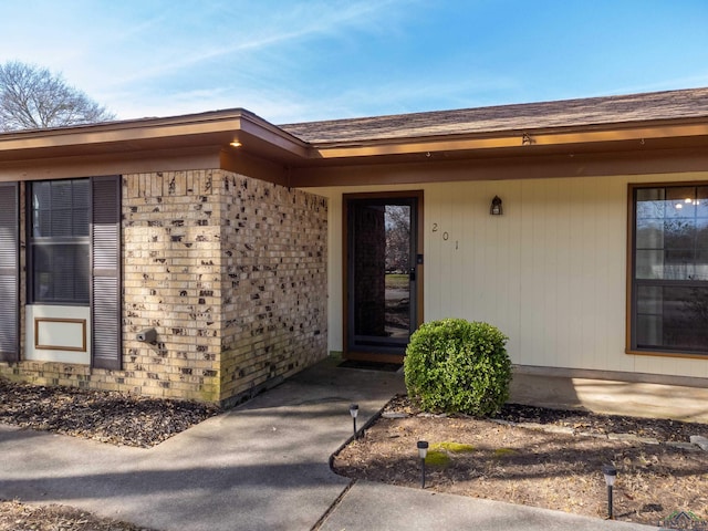 entrance to property with a shingled roof and brick siding