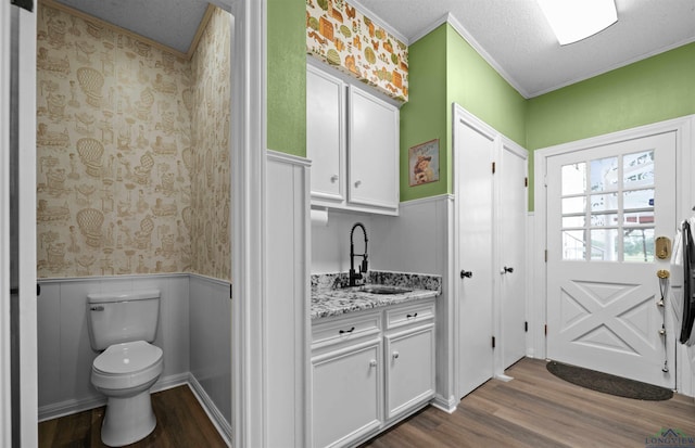 interior space with ornamental molding, a textured ceiling, vanity, hardwood / wood-style flooring, and toilet