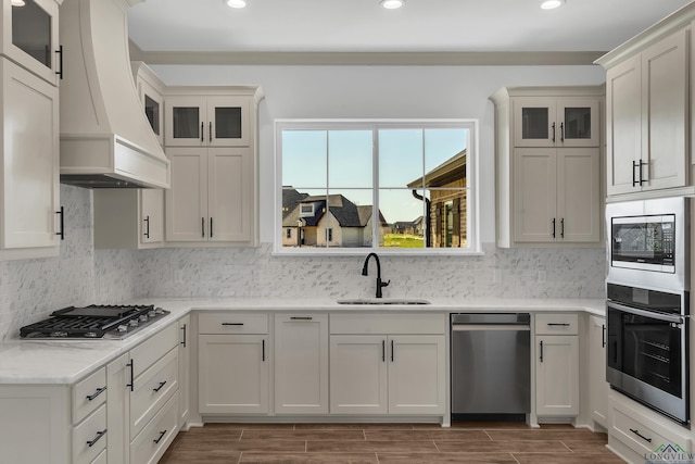 kitchen with white cabinetry, sink, tasteful backsplash, premium range hood, and appliances with stainless steel finishes