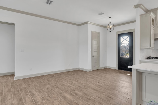 foyer featuring light wood-type flooring, ornamental molding, and an inviting chandelier