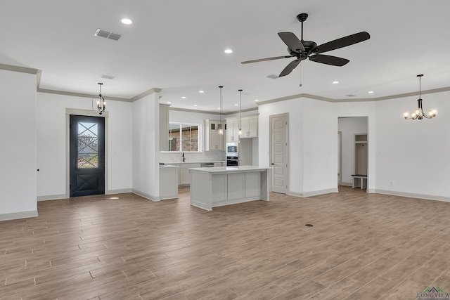 kitchen featuring ornamental molding, ceiling fan with notable chandelier, decorative light fixtures, white cabinetry, and a kitchen island