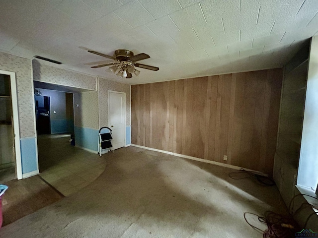 carpeted spare room with ceiling fan and wood walls