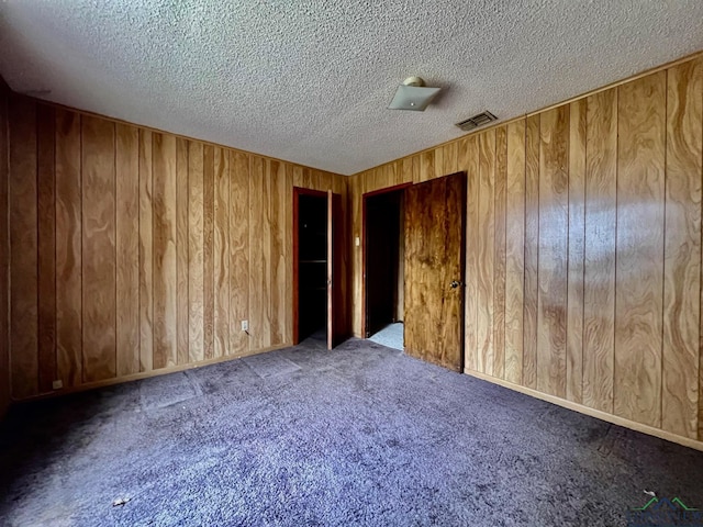 carpeted spare room with visible vents, wood walls, and a textured ceiling