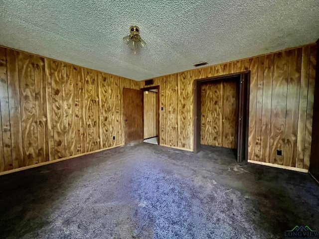 spare room featuring wooden walls, visible vents, a textured ceiling, and carpet flooring