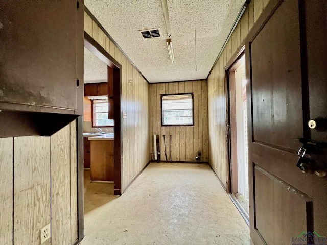 hallway featuring a sink, wood walls, visible vents, and a textured ceiling