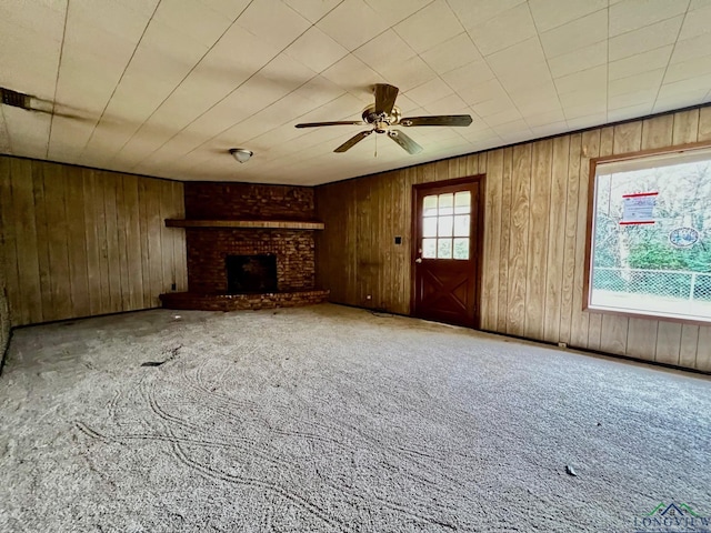 unfurnished living room with wood walls, ceiling fan, a fireplace, and carpet flooring