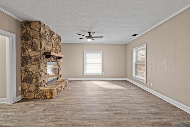 unfurnished living room featuring ceiling fan, ornamental molding, a healthy amount of sunlight, and a stone fireplace